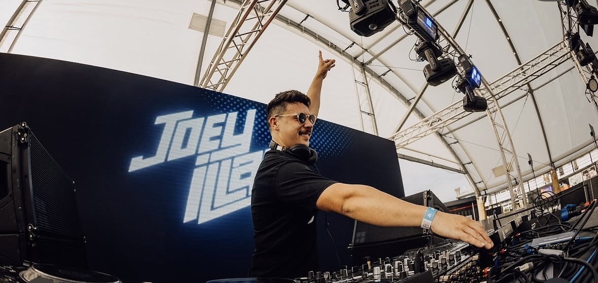 Joey iLLah reaching across the mixer with his name on the blue LED screen